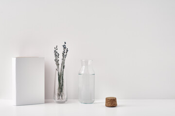 A transparent vase with lavender, a bottle of water with a cork stopper and a book on a white background. Minimalism, eco-materials in the interior decor. Copy space, mock up.