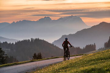 active woman riding her electric mountain bike at sunset in front of the awesome silhouette of Mount Saentis, Appenzell switzerland