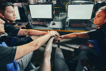 Professional multiracial cyber sport team putting hands together before starting eSports tournament