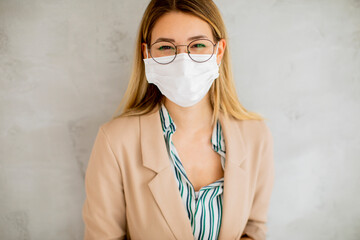 Young woman standning by the grey wall and wearing a respiratory mask from coronavirus disease