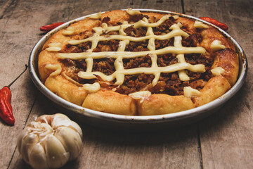 Pizza with beef and cream cheese surrounded by chilies and garlic served on wooden table