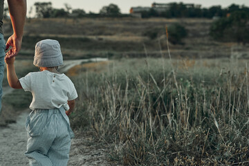 Two-year-old child in a hat walks along a country road, summer. Knowledge of the world.