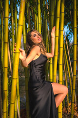 Lifestyle, blonde girl in a black dress in the park in nature, perched on beautiful bamboo, fashion in the bamboo trees