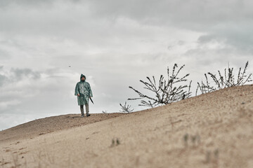 Cloudy sky and sand, in the background a man in a green raincoat. Travel in any weather.