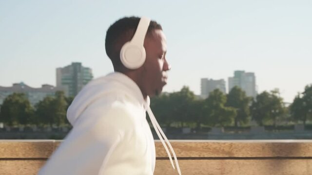 Side-view closeup of young african american man jogging in headphones with his eyes closed enjoying process in summer morning