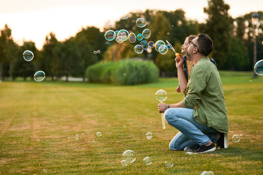 Young father and his little girl having fun while blowing soap bubbles on a summer day, daughter and dad spending time together outdoors