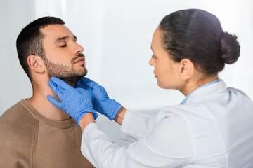 Obraz premium African american doctor in latex gloves examining throat of patient with closed eyes