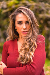 Fototapeta premium Autumn lifestyle, blonde Caucasian girl in a red sweater enjoying nature in a park. Portrait photo in nature