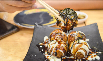 Hand holding chopsticks with hot takoyaki in japanese restaurant.tako yaki on black plate.
