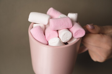 Woman's hand holding a pink glass filled with sweet marshmallows