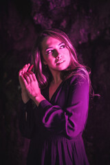 Lifestyle, a young Caucasian blonde in a black dress in a photo inside a cave, illuminated with pink led light. With soft diffuse light on the side