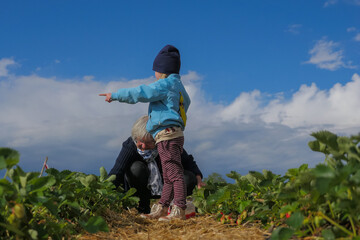 Child Standing and Pointing in Field with Grandmother Picking Crops