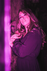 Lifestyle, a young Caucasian blonde in a black dress in a photo inside a cave, illuminated with pink led light. With soft diffuse light on the side