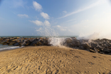 Rocky coastline with long waves lapping with sand and blue sky.