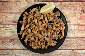Ration of fried chopitos (squid tips) in black plate on rustic wooden table