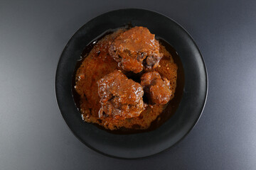 Ration of bullfighting oxtail stewed on black plate and black background