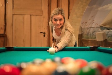 Attractive young blonde woman playing pool at the billiard table