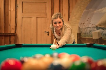 Attractive young blonde woman playing pool at the billiard table