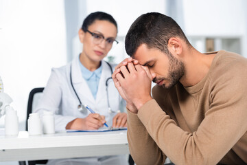 Female african american doctor looking at depressed patient, while sitting at workplace on blurred foreground