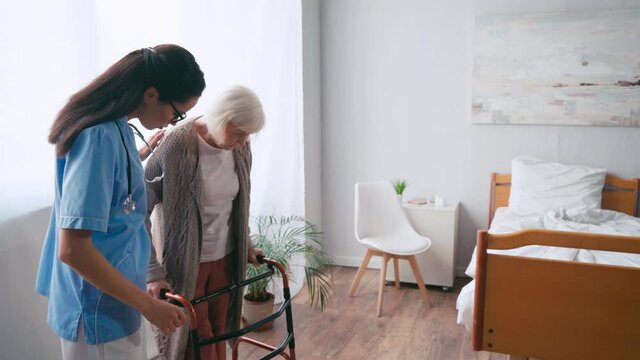 brunette geriatric sister helping woman stepping with walkers