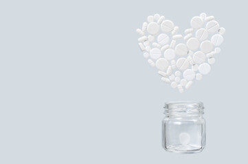 White medical pills in the shape of a heart fly out of a glass jar