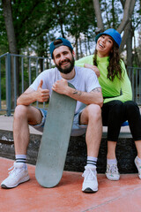 Couple having fun together with skateboard and showing thumb up