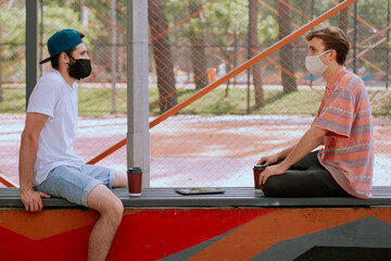 Closeup in front of the camera two men with mask enjoying the time outside in park talking about...