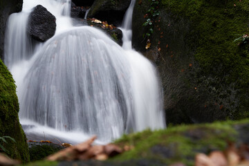 Closeup of a small cascade of a waterfall surrounded by rocks with moss. © Jan
