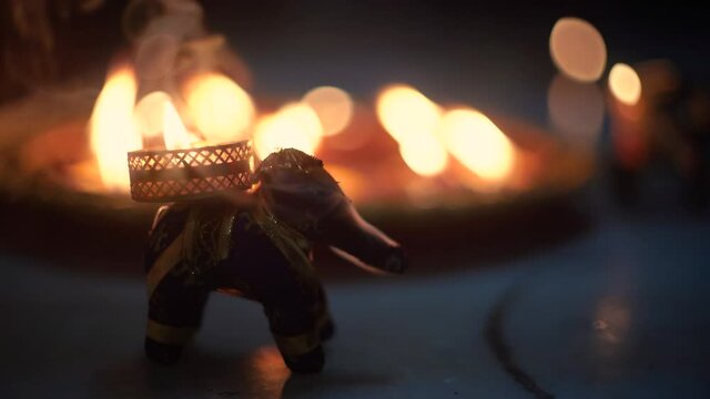 small elephant incense holder with smoke coming out and an out fo focus background with diya oil lamps lit behind it with flickering flames showing the hindu festival of diwali