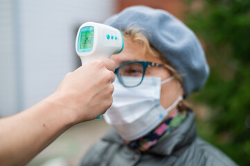 A doctor measures the temperature of an elderly woman wearing a mask with a non-contact infrared thermometer outdoors