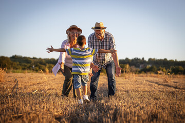 Grandparents having fun with the grandson. They're playing on the meadow and joying in sunset.	