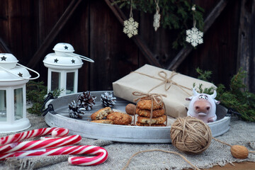 New year's composition: a tray with festive cookies, sweets, a gift, cones, a bull on a wooden background with a decorated branch-the concept of preparing pleasant surprises for relatives and friends