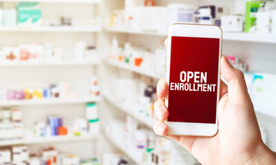 hand holding smart phone in pharmacy drugstore. Text OPEN ENROLLMENT
