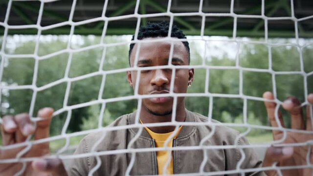 Frustrated young black man behind net outdoors in city, black lives matter concept.