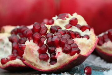 Broken pomegranate with bright red grains close-up on a background of whole pomegranate fruits on a wooden surface with snow outdoors in winter. A piece of broken pomegranate close-up.