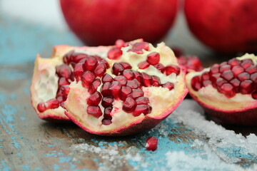 
Ruby pomegranate seeds outdoors.
 Open broken ripe pomegranate with burgundy red seeds on a background of whole pomegranates on a wooden surface in wet snow. Still life.