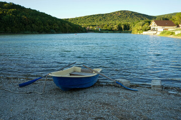 Fototapeta na wymiar a blue boat is moored on the shore of a lake against a beautiful landscape