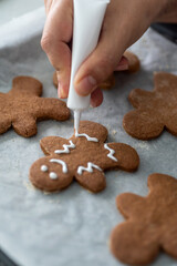 Fototapeta na wymiar Anonymous woman decorating some homemade gingerbread men cookies at kitchen