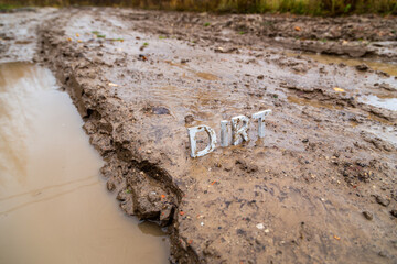 the word dirt composed of silver metal letters on wet clay surface