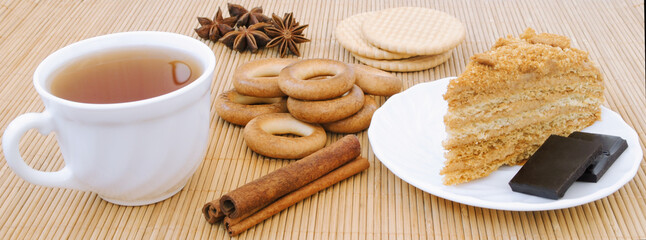 Still life of a glass with tea, cake, cookies, cinnamon sticks and anise on a bamboo napkin
