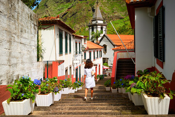 Fototapeta na wymiar Holiday in Madeira. Middle aged woman with long hair wearing a white dress watches blue hortensia flowers on street of Sao Vicente village, Madeira.