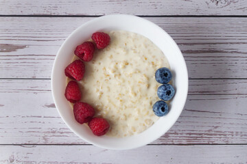 Oatmeal porridge with raspberries and blueberries in a white plate.