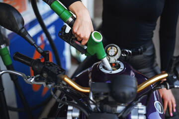Female's gentle hand is holding a fueling gun. Motorcycle's tank is fueling by female owner.