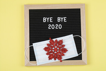 black letter board with text BYE BYE 2020 with mask and red snowflake on yellow background.
