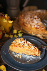 Homemade apple pie with fresh fruits, sugar powder, autumn yellow leaves. Selective focus, dark background, rustic wooden table, copy space. Organic freshly baked dessert.