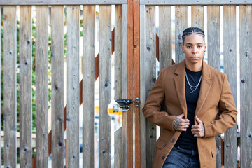 Strong, independent young black woman with long brown coat standing against a wood fence