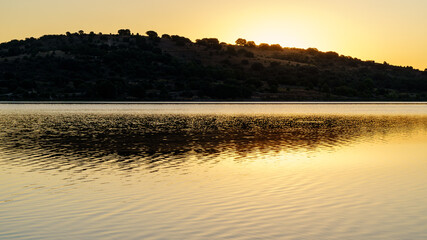 Amanecer en el lago con luz dorada saliendo por detr&aacute;s de la monta&ntilde;a y reflejo en el lago. Copy space.

