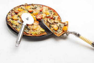 Slice of pizza on scoop. Ready pizza on black plate. Pizza cutter on pizza.