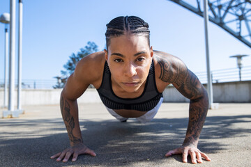 Fototapeta premium Strong black woman with tattoos doing pushups outside to build muscles