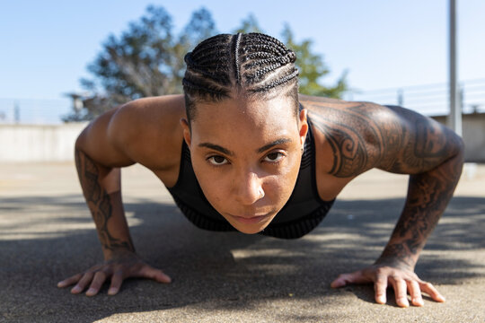 Strong black woman with tattoos doing pushups outside to build muscles